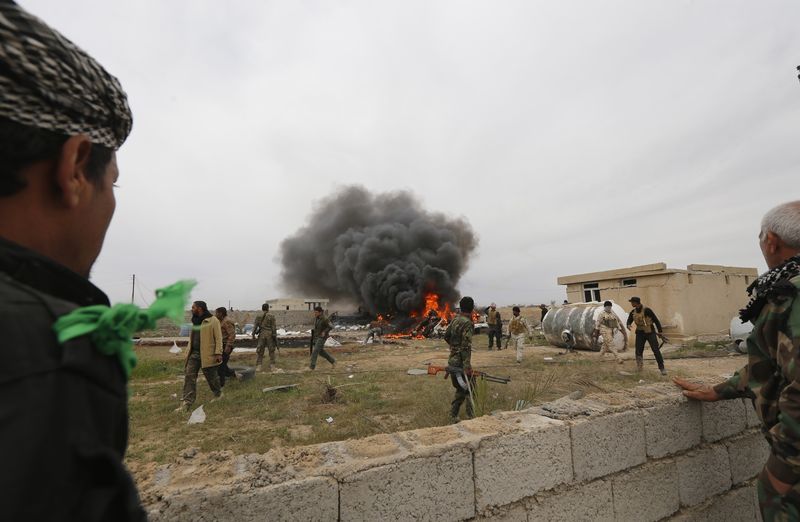 © Reuters. Combatentes xiitas conhecidos como Hashid Shaabi se reúnem enquanto fumaça sobe de veículo, perto de Tikrit