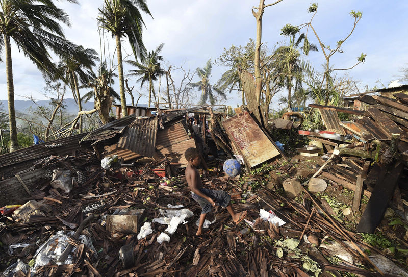 © Reuters. A boy called Samuel kicks a ball as his father Phillip searches through the ruins of their home which was destroyed by Cyclone Pam in Port Vila