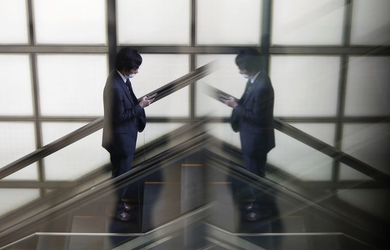 © Reuters. Man with a smartphone riding on an escalator is reflected in a glass window at a business district in Tokyo