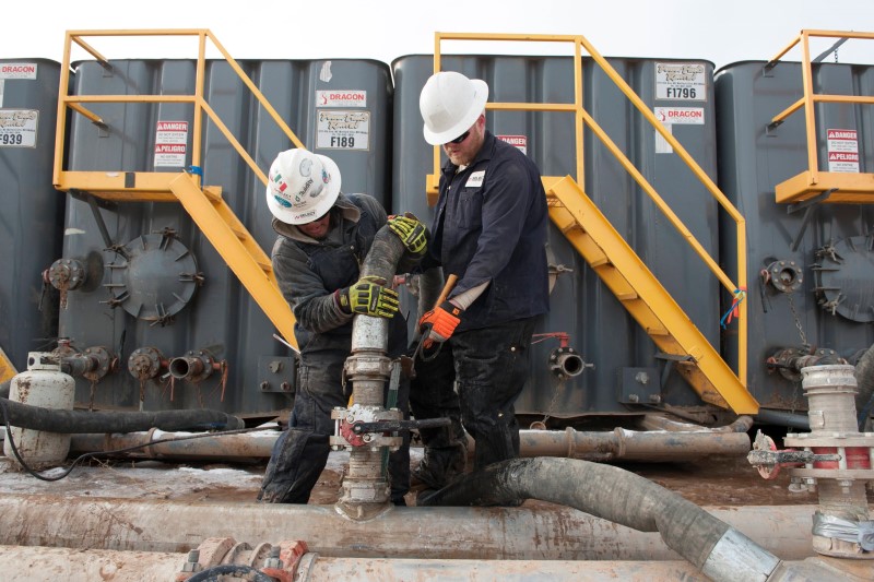 © Reuters. Mody Torres and Josh Anderson of Select Energy Services connect hoses between a pipeline and water tanks at a Hess fracking site near Williston