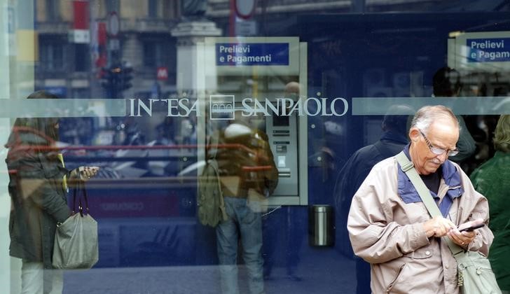 © Reuters. A man stands outside a building as people use Intesa Sanpaolo automated teller machines (ATMs) in Milan