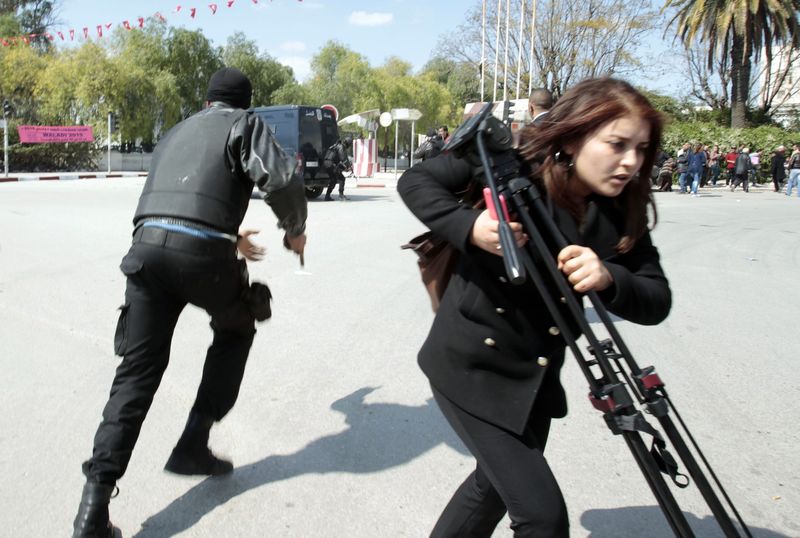 © Reuters. Police officers and a journalist run outside the parliament in Tunis