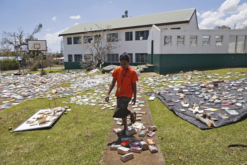 © Reuters. Teacher walks past library books laid out to dry in the sun after the roof of the school library was blown away by Cyclone Pam at the Central School in Port Vila