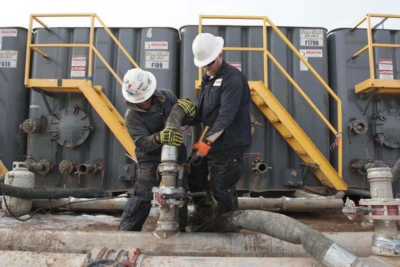 © Reuters. Mody Torres and Josh Anderson of Select Energy Services connect hoses between a pipeline and water tanks at a Hess fracking site near Williston