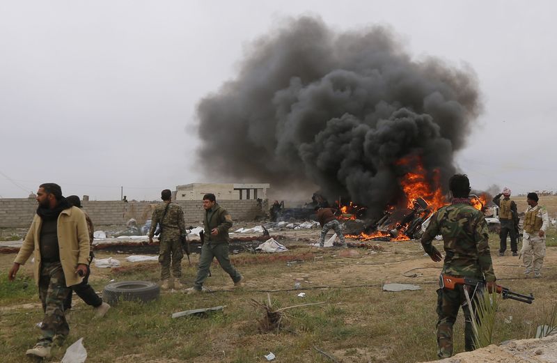 © Reuters. Shi'ite fighters known as Hashid Shaabi walk with their weapons as smoke rises from an explosives-laden military vehicle driven by an Islamic State suicide bomber, which exploded during an attack on the southern edge of Tikrit