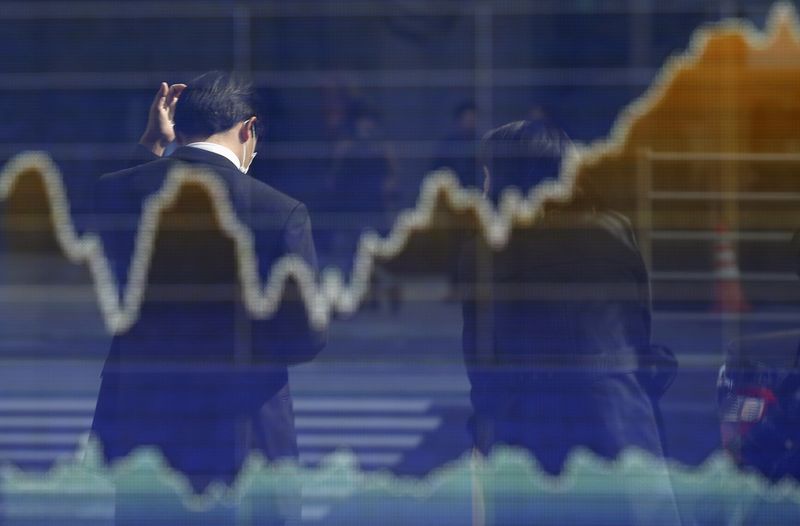 © Reuters. Man is reflected on an electronic board displaying a graph of Japan's Nikkei share average outside a brokerage in Tokyo