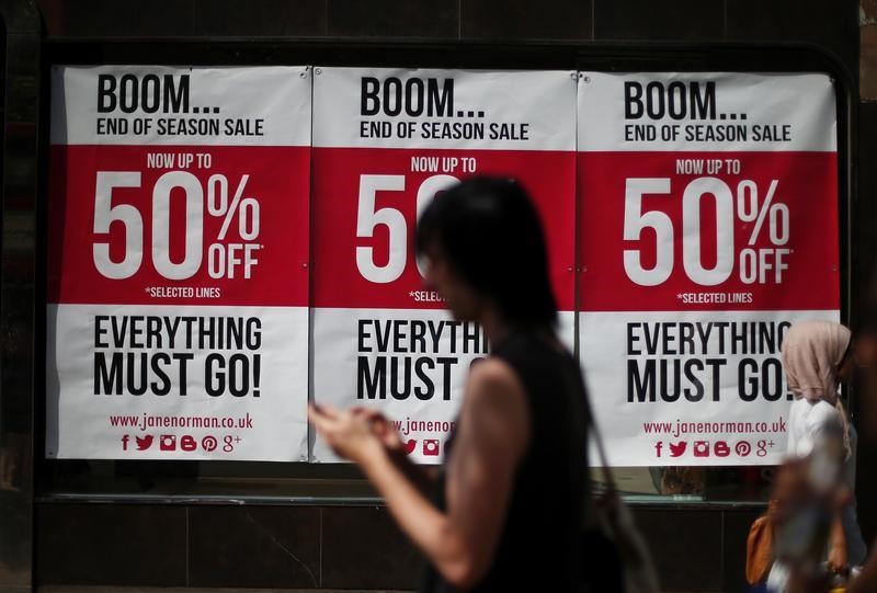 © Reuters. A man checks his mobile phone as he passes sale advertising in a shop window on Oxford Street in London