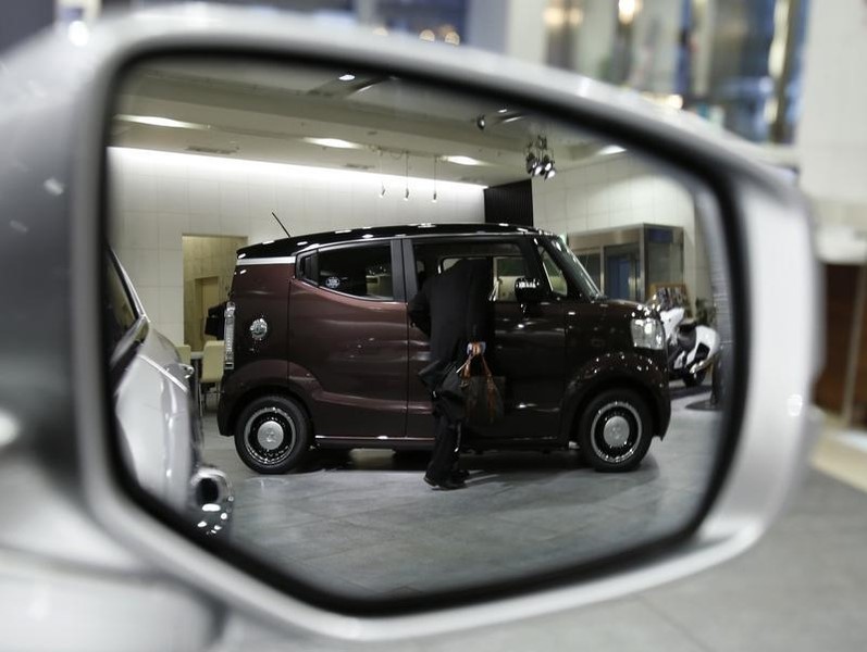 © Reuters. A man looking at the interior of Honda Motor Co's N-BOX SLASH vehicle is reflected in a side mirror of a car displayed at the company showroom in Tokyo