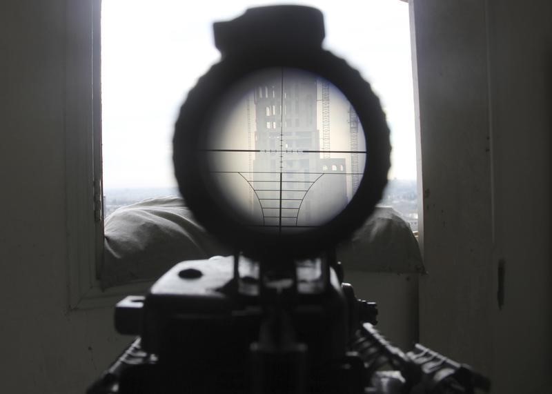 © Reuters. A view seen through the scope of a weapon belonging to a sniper and rebel fighter shows a building where forces loyal to Syria's President Bashar al-Assad are stationed, as seen from Al Waer