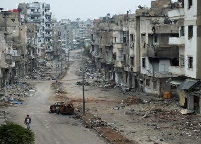 © Reuters. A man walks past a burnt car and damaged buildings along a street at the al-khalidiya neighbourhood of Homs