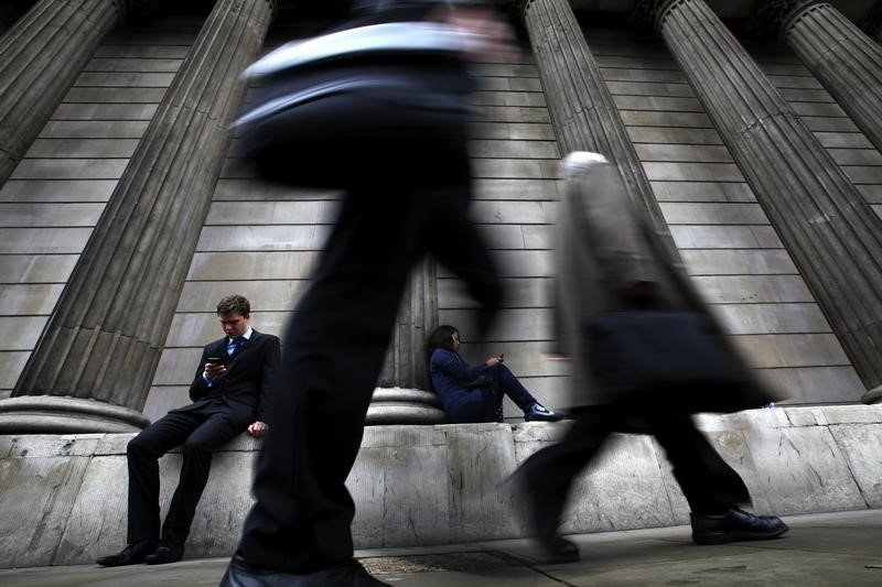 © Reuters. A man and woman use their mobile phones as commuters walk past the columns of the Bank of England in the City of London