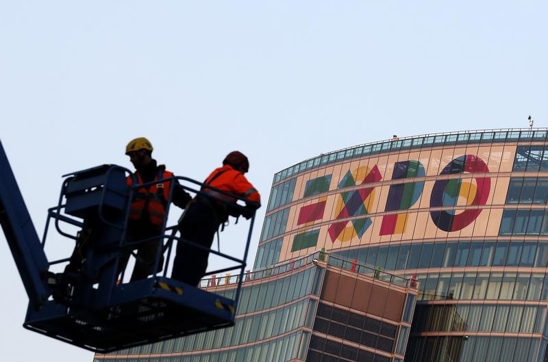 © Reuters. Lavoratori su una gru a Milano davanti al palazzo della Regione Lombardia, col logo di Expo 2015 