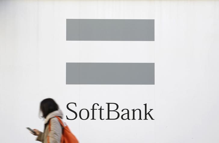 © Reuters. A woman using a mobile phone walks past the logo of SoftBank Corp in Tokyo