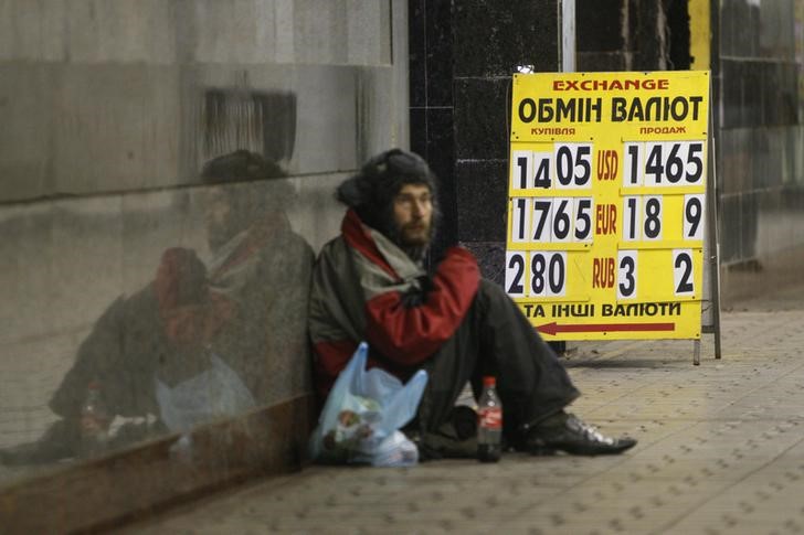 © Reuters. A homeless man sits near a board showing currency exchange rates in Kiev