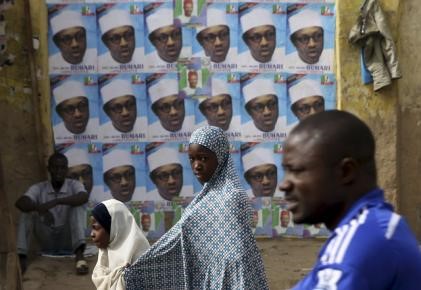 © Reuters. People walk in front of election posters of presidential candidate Muhammadu Buhari in Kano