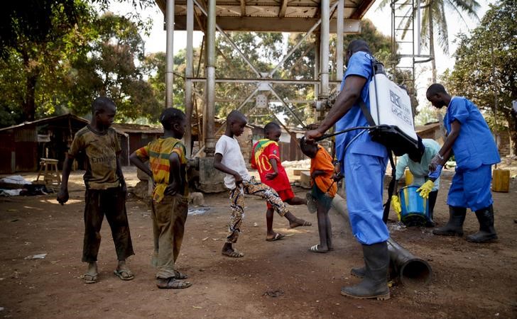 © Reuters. Children come forward to get their feet disinfected after a Red Cross worker explained that they are spraying bleach, and not spraying the village with the Ebola virus, in Forecariah 