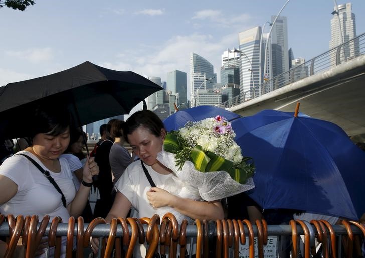 © Reuters. People pick up free umbrellas as they queue up to pay their respects to the late first prime minister Lee Kuan Yew at the Padang grounds outside the Parliament House in Singapore