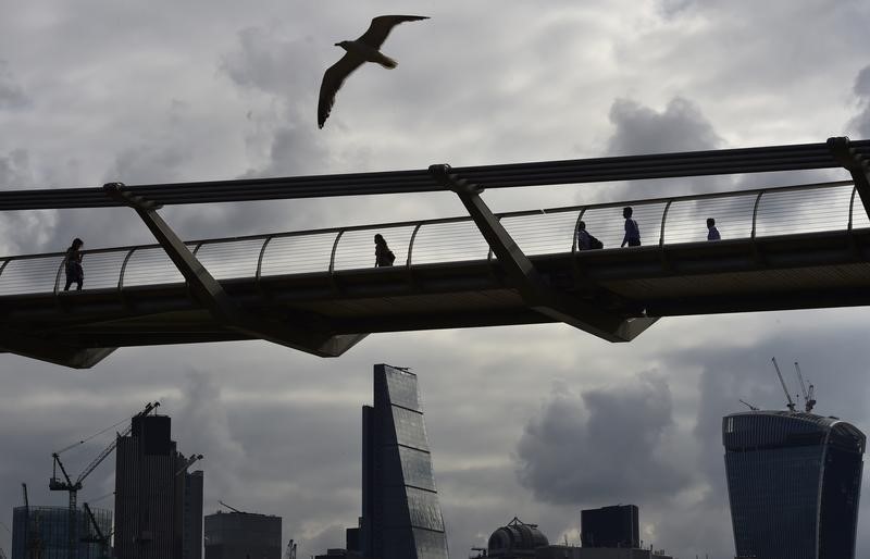 © Reuters. Workers cross the Millenium Bridge with the City of London seen behind, in London