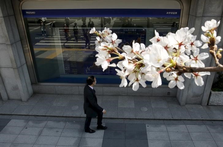 © Reuters. A Tokyo businessman looks at an electronic stock quotation board, as cherry blossoms bloom, outside a brokerage in Tokyo