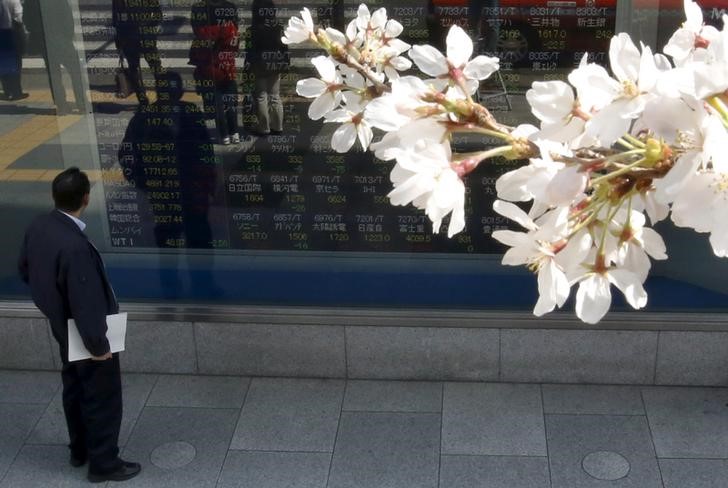 © Reuters. A Tokyo businessman look at an electronic stock quotation board, as cherry blossoms bloom, outside a brokerage in Tokyo