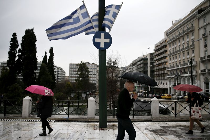 © Reuters. People holding umbrellas make their way next to fluttering Greek national flags on the main Constitution (Syntagma) square during heavy rainfall in Athens