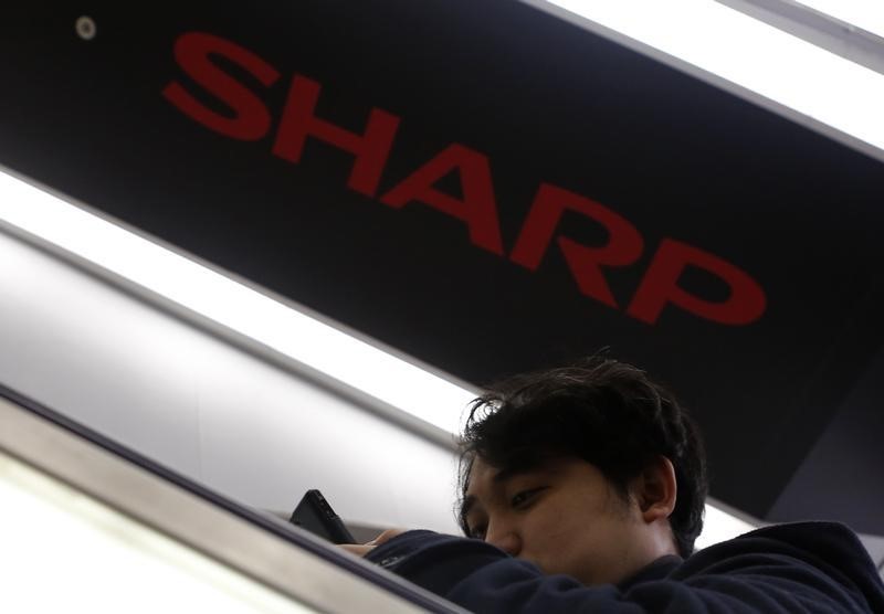 © Reuters. Shopper using a smartphone rides an escalator past under a logo of Sharp Corp at an electronics shop in Tokyo