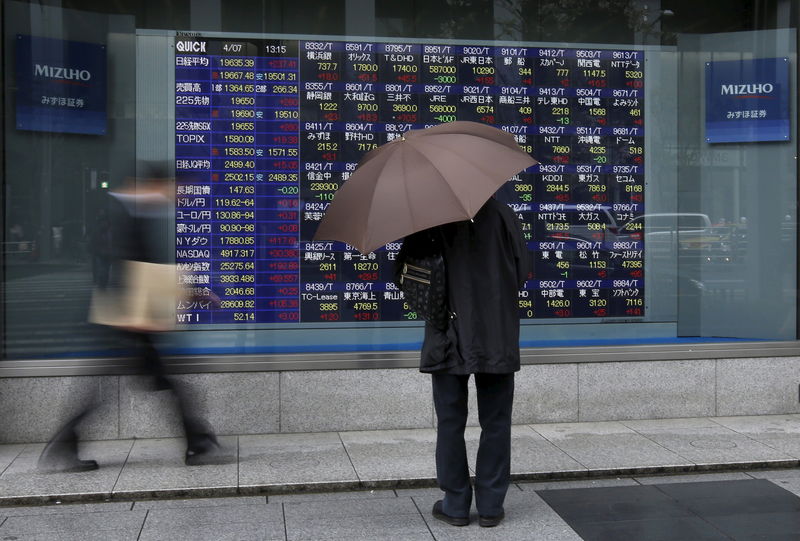 © Reuters. A man holding an umbrella looks at an electronic stock quotation board outside a brokerage in Tokyo