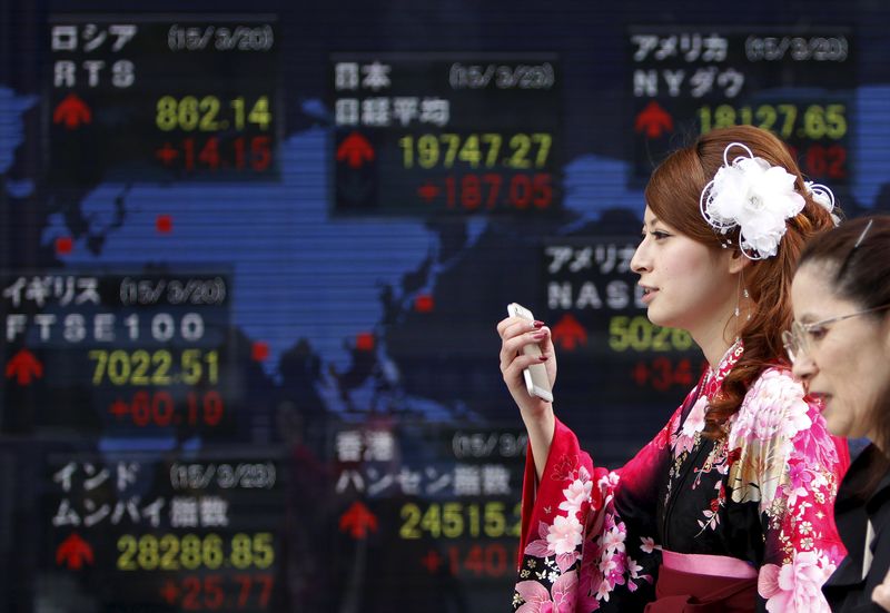 © Reuters. A woman wearing a Hakama, or Japanese traditional Kimono, holds her mobile phone as she walks past an electronic board, showing the stock market indices of various countries, outside a brokerage in Tokyo