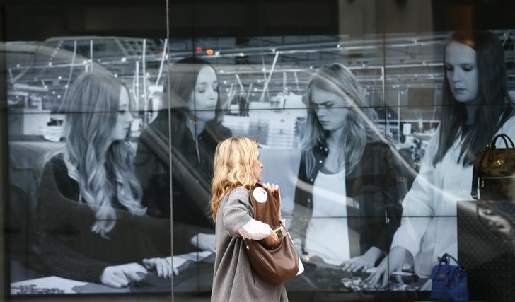 © Reuters. A woman reaches into her handbag as she walks past a video display in the shop window of a Mulberry store in central London