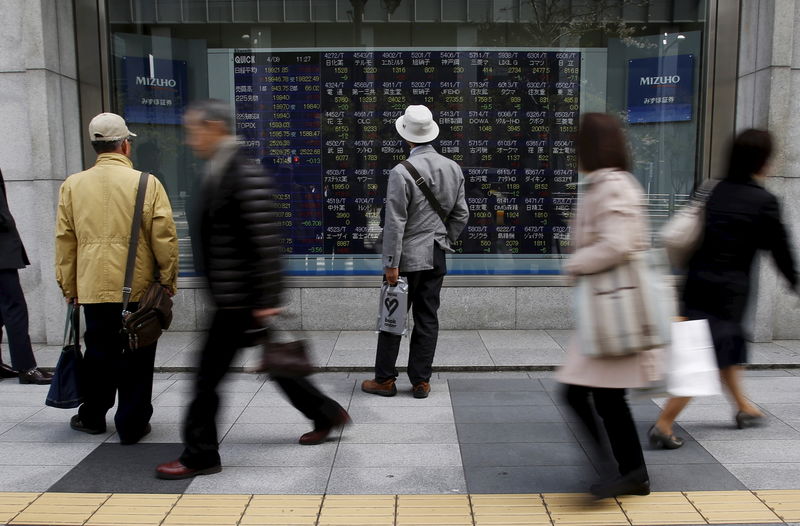 © Reuters. Pedestrians look at an electronic board showing the various stock prices outside a brokerage in Tokyo