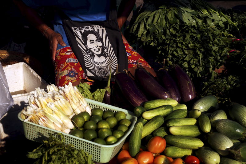 © Reuters. A vendor carrying a bag with a picture of Aung San Suu Kyi sells vegetables in downtown Yangon