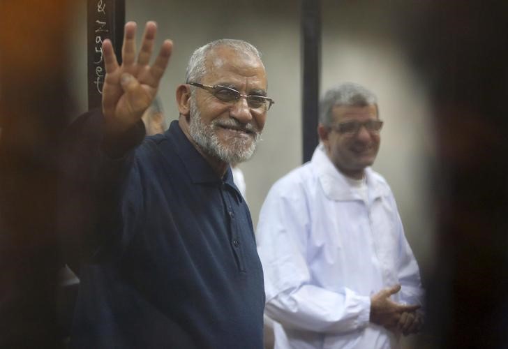 © Reuters. Muslim Brotherhood's Supreme Guide Mohamed Badie flashes the Rabaa sign as he stands behind bars during his trial with ousted Egyptian President Mohamed Mursi and other leaders of the brotherhood at a court on the outskirts of Cairo