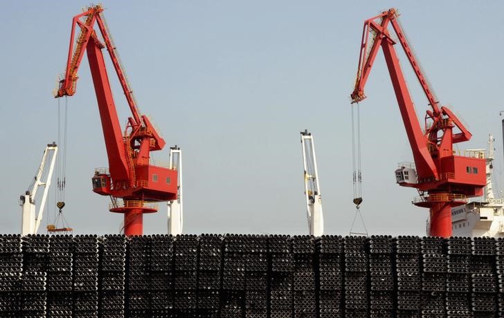 © Reuters. Piles of steel pipes to be exported are seen in front of cranes at a port in Lianyungang