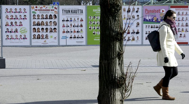 © Reuters. A woman walks past campaign posters of candidates in the Finnish Parliamentary elections put up along a street in Helsinki