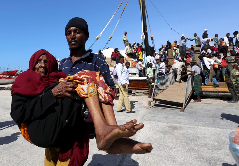 © Reuters. A man carries an elderly woman from a ship that has arrived, carrying people fleeing violence in Yemen, at the port of Bosasso in Somalia's Puntland region