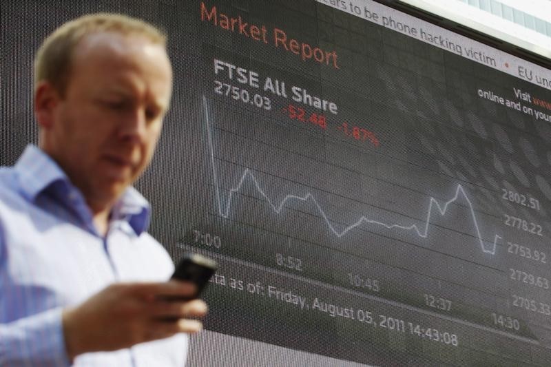 © Reuters. A man passes a screen showing the activity of the FTSE index at Canary Wharf financial district in London