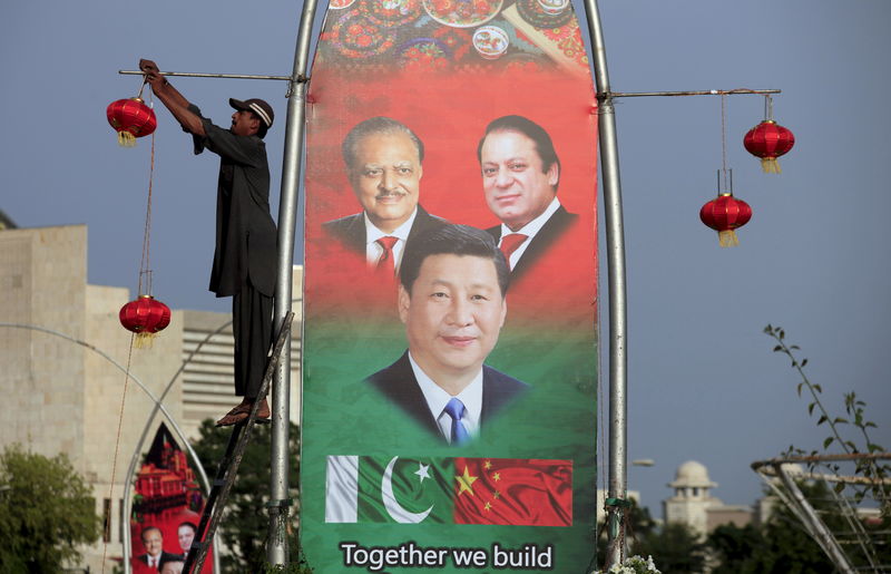 © Reuters. A man hangs decorations on a pole next to a banner showing Pakistan's President Hussain, China's President Xi and Pakistan's PM Sharif, ahead of Xi's visit to Islamabad