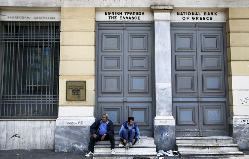 © Reuters. Two men sit in front of a National Bank branch in central Athens