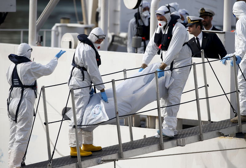 © Reuters. Italian coastguard personnel in protective clothing carry the body of a dead immigrant off their ship Bruno Gregoretti in Senglea