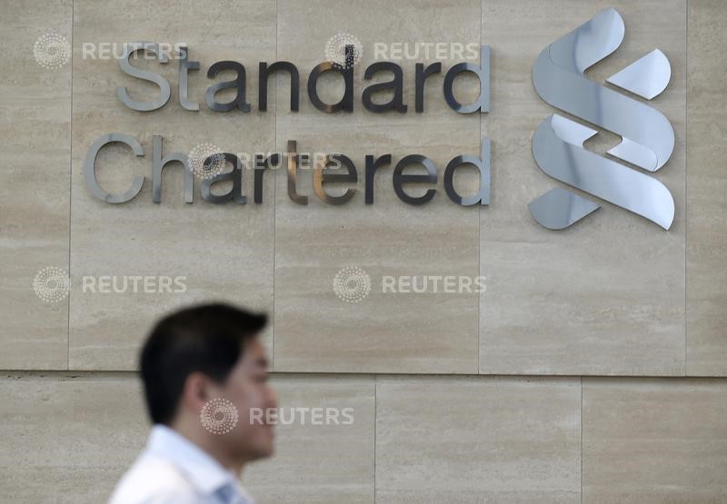 © Reuters. An office worker walks past a Standard Chartered logo outside its head office in Singapore