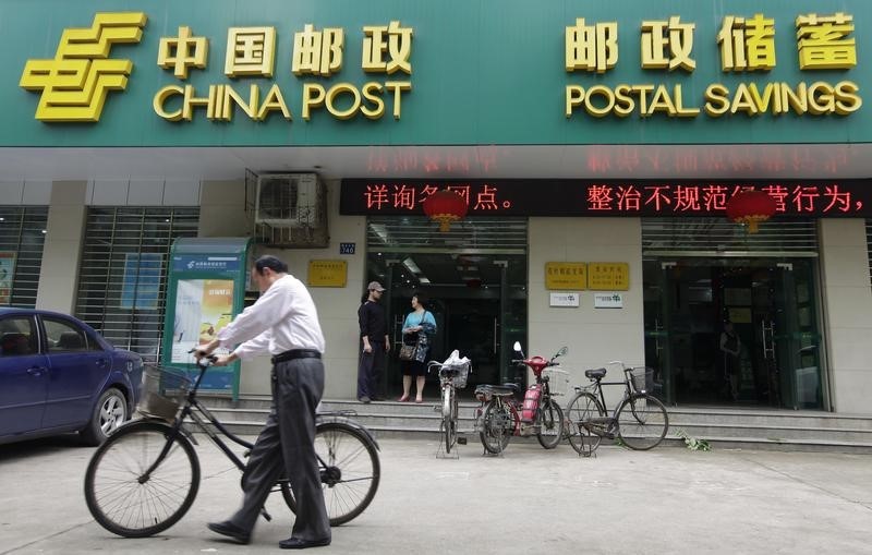 © Reuters. A man pushes his bicycle past a branch of China Post's Postal Savings Bank of China in Wuhan