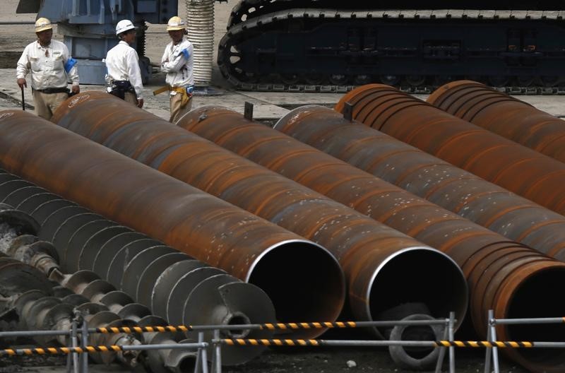 © Reuters. Workers stand next to steel pipes at a construction site in Tokyo