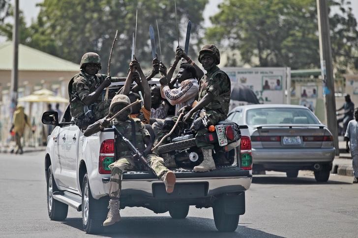 © Reuters. Soldiers and people carrying machetes ride on the back of a vehicle along a street in Gombe