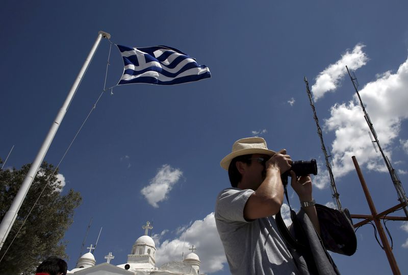 © Reuters. Tourist takes pictures as a Greek national flag flutters above the Orthodox church of Saint George, atop Lycabetus hill in Athens