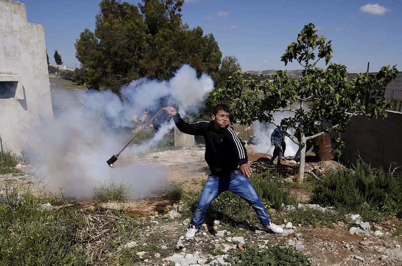 © Reuters. A Palestinian protester uses a sling to return a tear gas canister fired by Israeli troops during clashes following a protest against Jewish settlements in Nabi Saleh