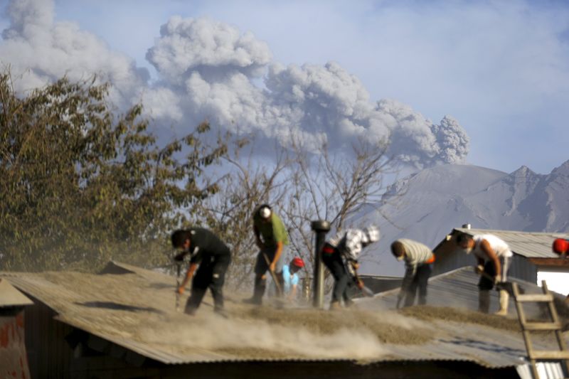 © Reuters. People clean an ash-covered roof of a house in Ensenada town