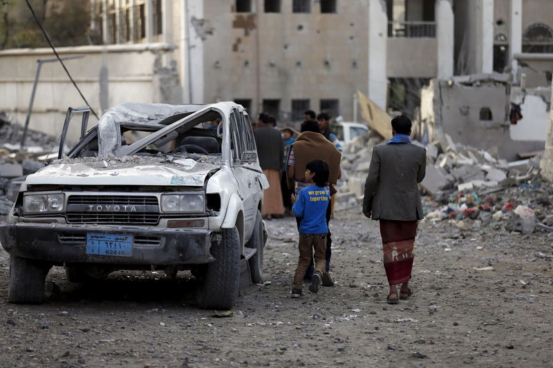 © Reuters. People walk past a car damaged by an air strike in Sanaa