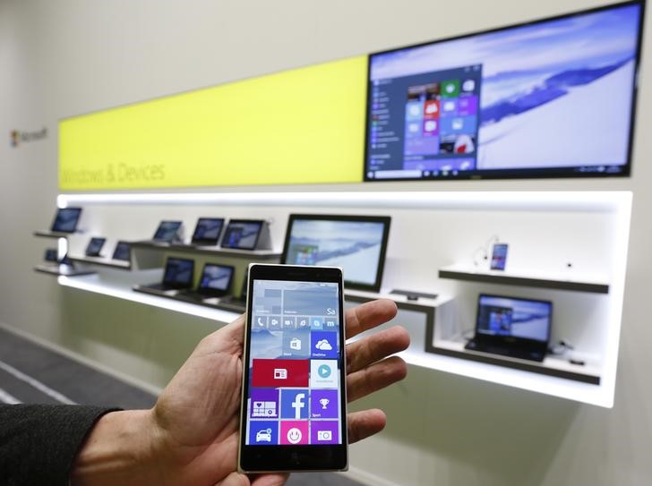 © Reuters. A Microsoft representative holds a Windows smartphone with Windows 10 operating system in front of other devices with Windows 10 at the CeBIT trade fair in Hanover