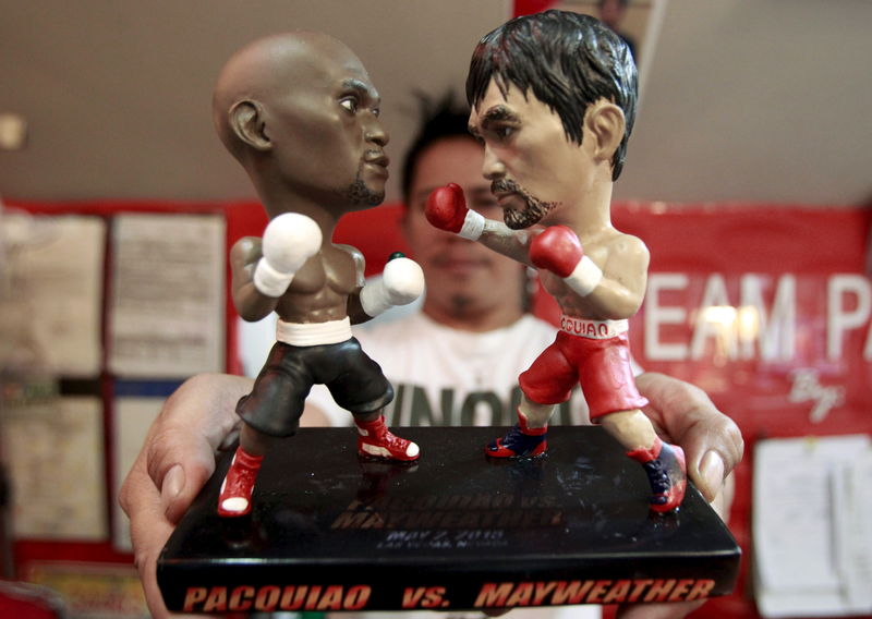 © Reuters. Store employee holds up a stand with miniature figurines of boxers Pacquiao of the Philippines and Mayweather Jr. of the U.S., at a mall in Manila 