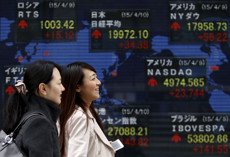 © Reuters. Pedestrians walk past an electronic board showing the stock market indices of various countries outside a brokerage in Tokyo